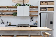 a white beach kitchen with a white tile backsplash and cabinets, open shelves, crates, a woven pendant lamp and wooden stools