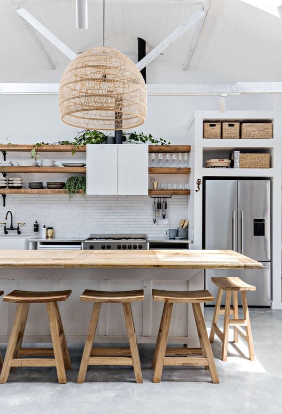 a white beach kitchen with a white tile backsplash and cabinets, open shelves, crates, a woven pendant lamp and wooden stools
