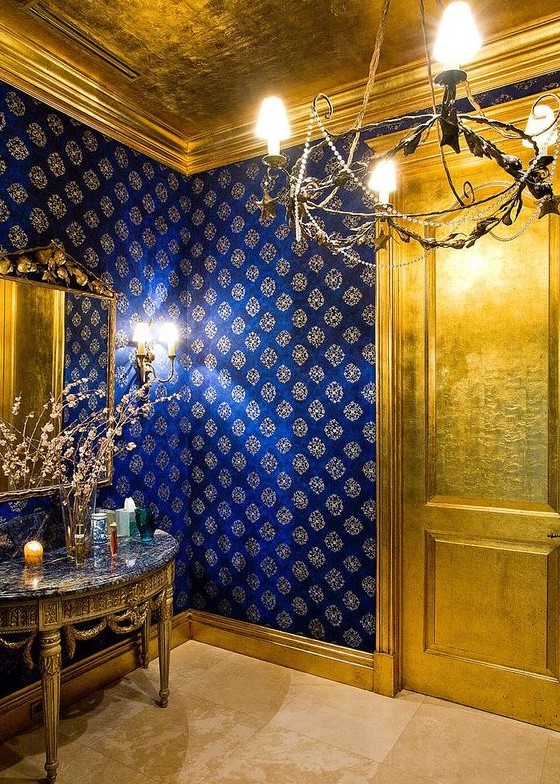 an exquisite and super chic powder room done with a gold door, a gold vanity and a ceiling that matches