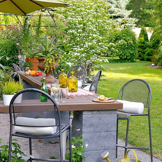 an outdoor cooking and dining space with a concrete and wood corner table and metal stools is a lovely and comfy space