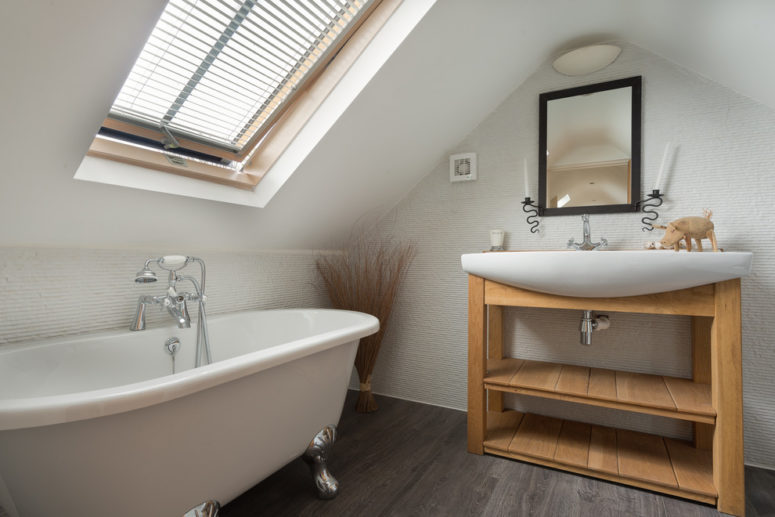 a modern attic bathroom with a wooden vanity, a clawfoot bathtub, a sink and a blinded window  (Colin Cadle Photography)