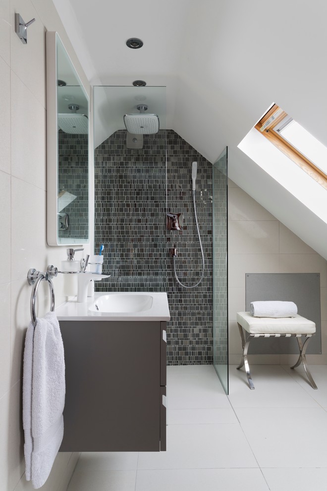 a contemporary attic bathroom with a grey tile wall in the shower, a grey floating vanity and a small stool  (Ripples Bournemouth)