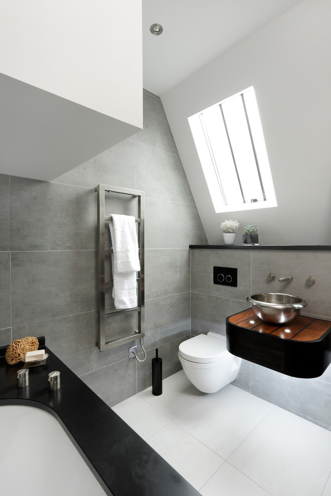 a bold attic bathroom with grey tiles, a black small vanity, a black clad tub and a white floor  (CUBIC Studios Limited)