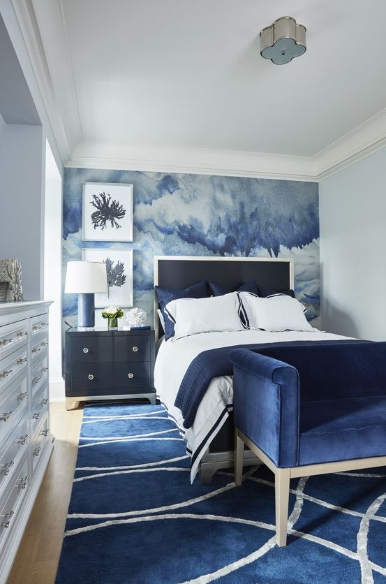 a bold bedroom with a watercolor blue accent wall and navy furniture and a rug for a sea-inspired feel