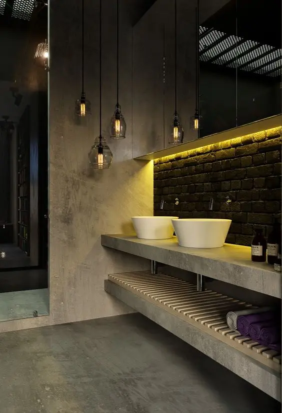 a catchy industrial bathroom of concrete, with a black brick backsplash, a concrete vanity and a cluster of pendant lamps