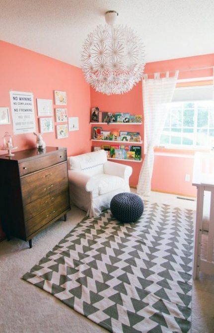 a cheerful grey and coral nursery with coral walls, a printed rug, a stained sideboard, a cool chandelier and whiet touches