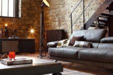 a chic living room with a leather sofa, a wood and metal coffee table on casters, a metal staircase and brick walls
