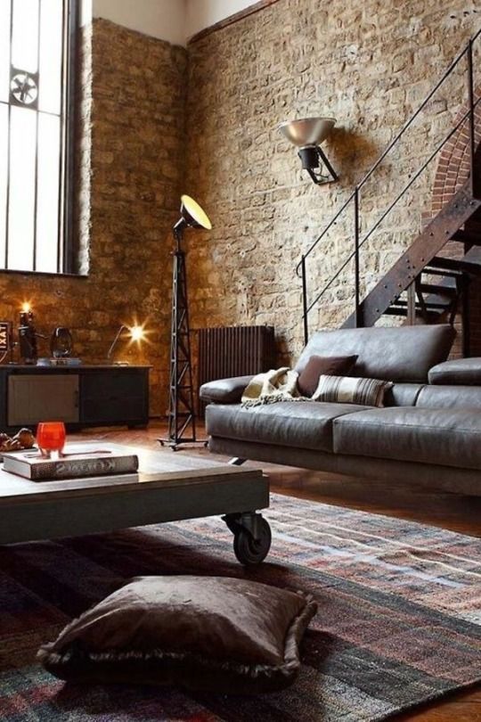 a chic living room with a leather sofa, a wood and metal coffee table on casters, a metal staircase and brick walls