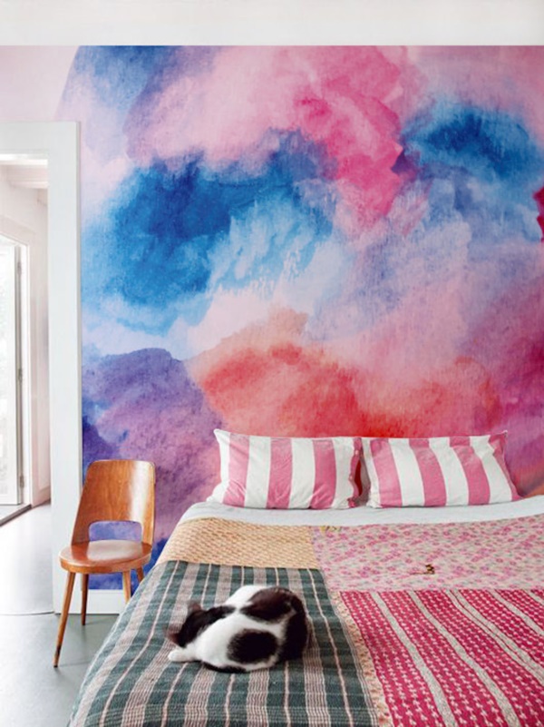 a colorful bedroom with a super bright watercolor wall, a bed with colorful bedding, a stained chair is amazing