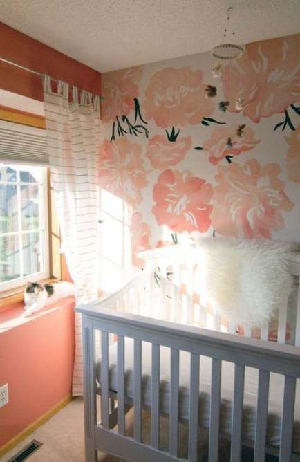 a colorful nursery with a floral statement wall, coral walls, a grey crib and white textiles to refresh the space