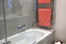 a contemporary bathroom with geometric print walls and floors, bright coral towels and a basket for storage