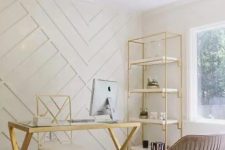 a glam home office with a white paneled geometric wall, a gold etagere, desk and chair, a blush chair and a bold chandelier