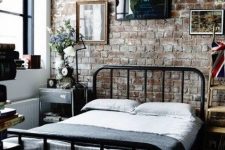 a laconic industrial bedroom with brick walls, a metal bed, mismatching nightstands, a gallery wall and vintage decor