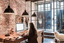 a large industrial home office with wooden beams and a brick wall, a large wooden desk and metal pendant lamps