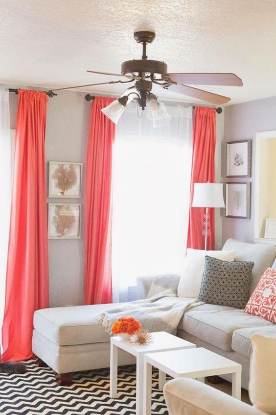 a living room with dove grey walls, coral curtains and pillows, a creamy sofa and white coffee tables