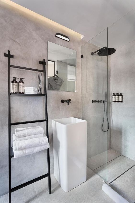 a minimalist industrial bathroom done of concrete, with built-in lights, a ladder and black fixtures