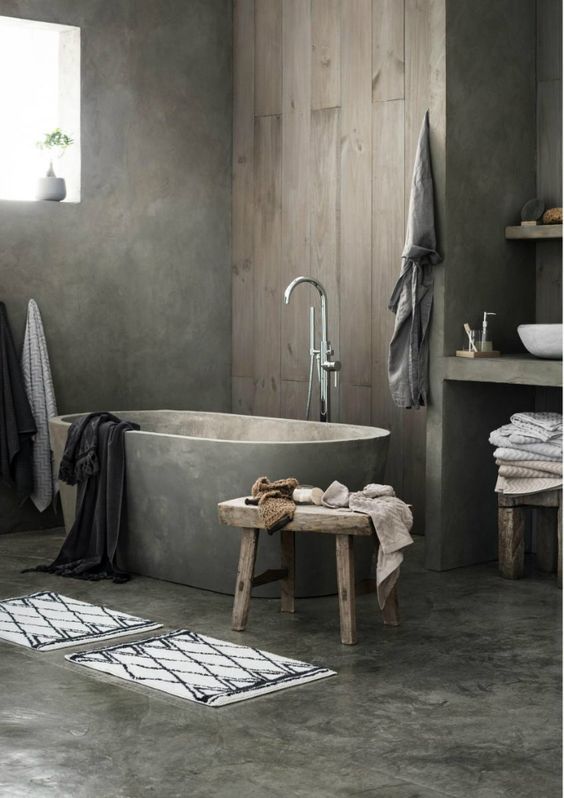 a minimalist industrial bathroom with concrete walls and a floor, a wooden wall, concrete vanities and a bathtub, wooden stools