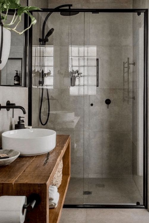 a modern industrial bathroom done with concrete, with a glass-enclosed shower space, a wooden vanity, a round sink and black fixtures