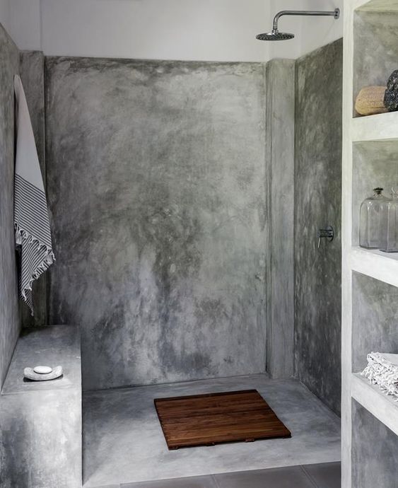 A modern industrial bathroom with concrete walls and a floor, a built in shelving unit and exposed pipes