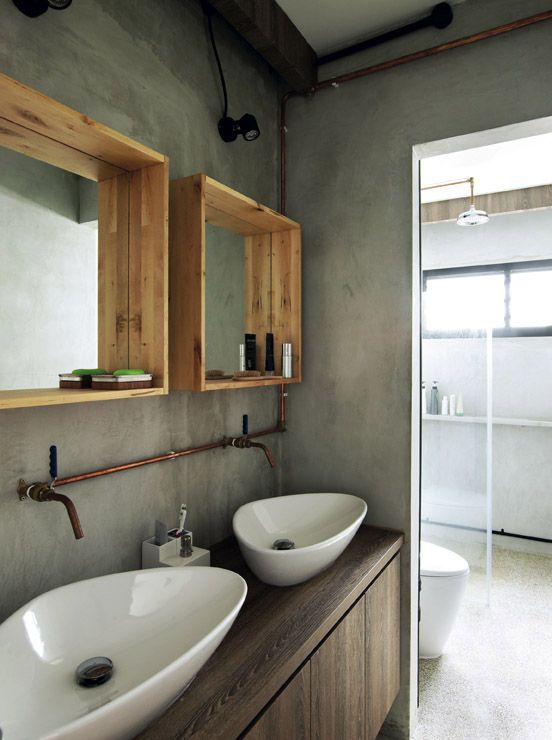 a modern industrial space with concrete walls, a wooden vanity, exposed copper pipes and wooden box mirrors