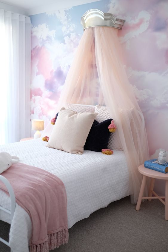 a pastel kid's room with a watercolor accent wall, a metal bed with a blush canopy and some side tables