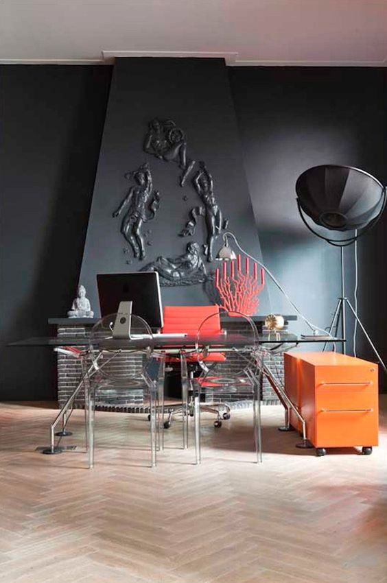 a quirky home office with graphite grey walls and a lamp, an industrial desk and acrylic chairs and touches of coral pink