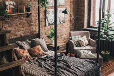 a small yet chic industrial bedroom with red brick walls, a canopy bed, potted greenery and lights plus catchy textiles