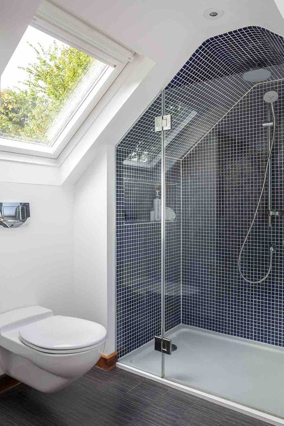 a tiny attic bathroom with navy tiles and white grout, a grey floor and a skylight