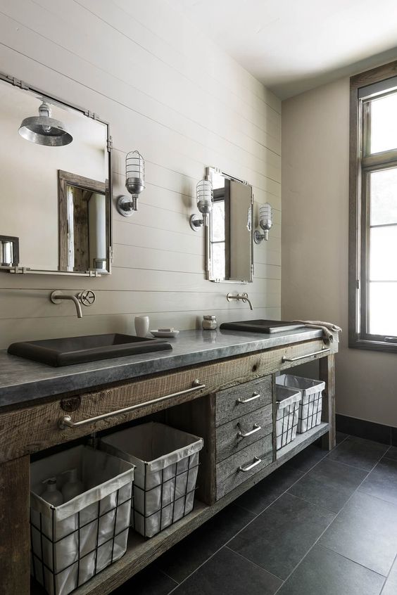 a vintage industrial bathroom with beadboard walls, a rough wood and stone vanity, stone sinks, exposed pipes and sconces