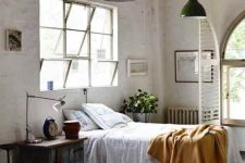 a vintage industrial bedroom with white brick walls, a bed with neutral bedding, green pendant lamps, a vintage wooden nightstand and table lamps