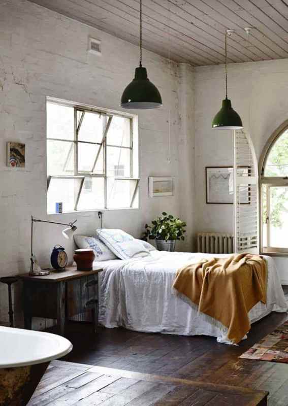 a vintage industrial bedroom with white brick walls, a bed with neutral bedding, green pendant lamps, a vintage wooden nightstand and table lamps