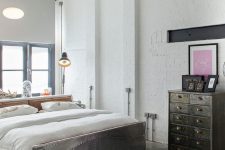 a white industrial bedroom with brick walls, a catchy metal bed, a vintage file cabinet for storage and pendant lamps