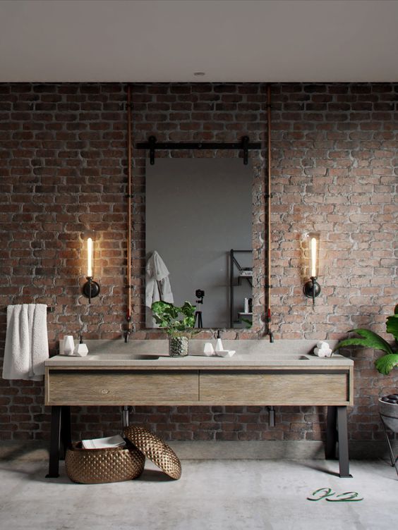 an industrial bathroom with brick walls, a wooden vanity with a stone sink, exposed pipes and wall sconces