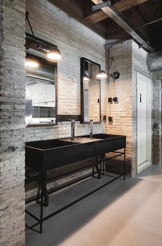an industrial bathroom with whitewashed walls, black metal vanity with sinks, mirrors, exposed pipes and lamps