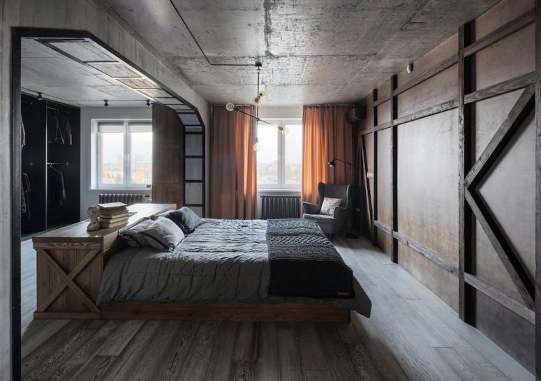 an industrial bedroom with a concrete ceiling and walls, a large wardrobe with a sliding wooden door, a wooden bed with grey bedding and yellow curtains