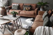 an industrial boho living room with leather sofas, potted plants, hairpin leg coffee tables and jute decor