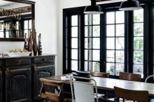 an industrial dining zone with a black vintage credenza, a stained table, mismatching chairs and black metal pendant lamps