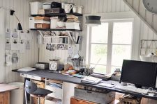 an industrial home office with shiplap walls and a whitewashed floor, a shared desk with mismatching stools and black shelves