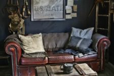 an industrial living room with a leather sofa, a shabby wooden chest and stool and some vintage art