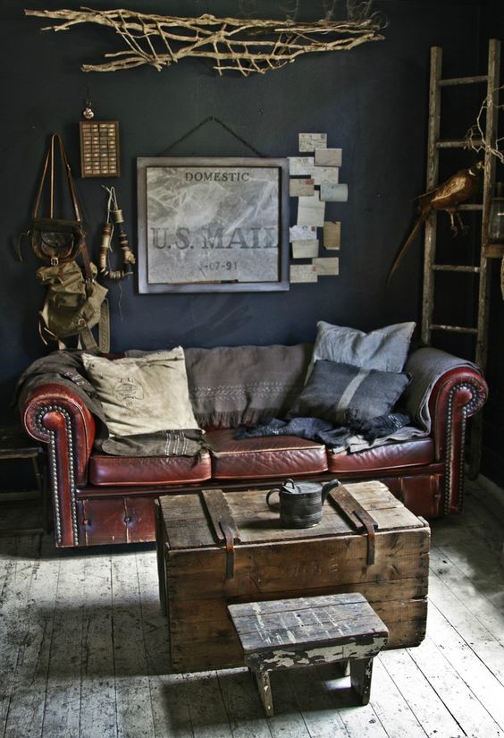 an industrial living room with a leather sofa, a shabby wooden chest and stool and some vintage art