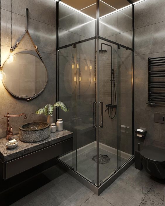 an industrial modern bathroom clad with grey tiles, with a glazed shower space, a floating vanity, copper faucets and exposed pipes