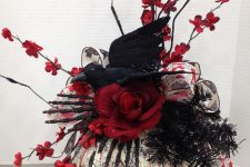 a Halloween centerpiece of a painted pumpkin, black glitter skeleton hands, red blooming branches, blooms and a crow on top
