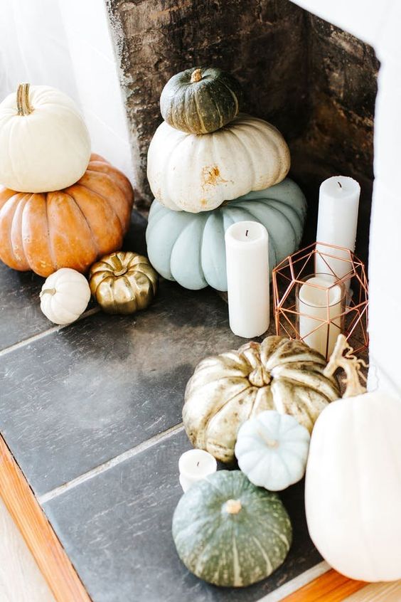 a Thanksgiving fireplace with stacked heirloom pumkins and pilalr candles in lanterns and without them