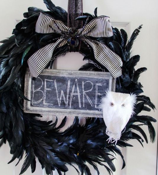 a black Halloween wreath of black feathers, a sign, a white owl and a black and white striped bow is amazing for decor