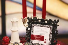 a black and red dessert table with a tray with red candles, chess, cupcakes topped with photos and a refined black frame