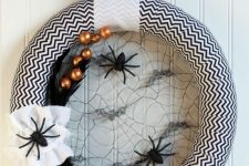a black and white Halloween chevron wreath with spider webs, spiders and feathers plus oversized beads is a cool idea to decorate your front door