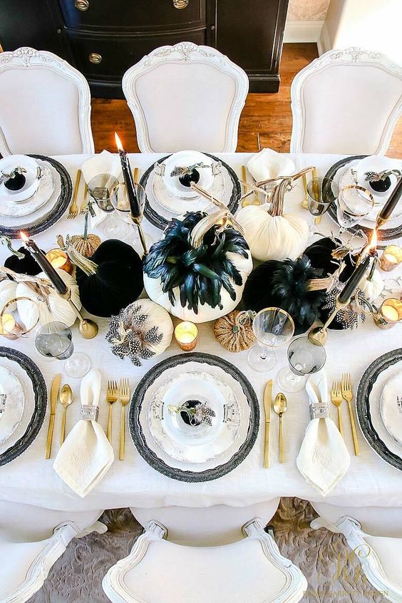 a chic Halloween tablescape with black and white pumpkins, feathers, candles, gold cutlery and candleholders