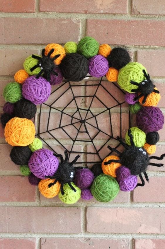 a colorful Halloween wreath of colorful yarn balls, yarn spiders and a spider web in the center is a cool and fun idea to decorate