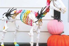 a colorful unicorn skeleton with bright stacked pumpkins is a unique Halloween decoration to rock