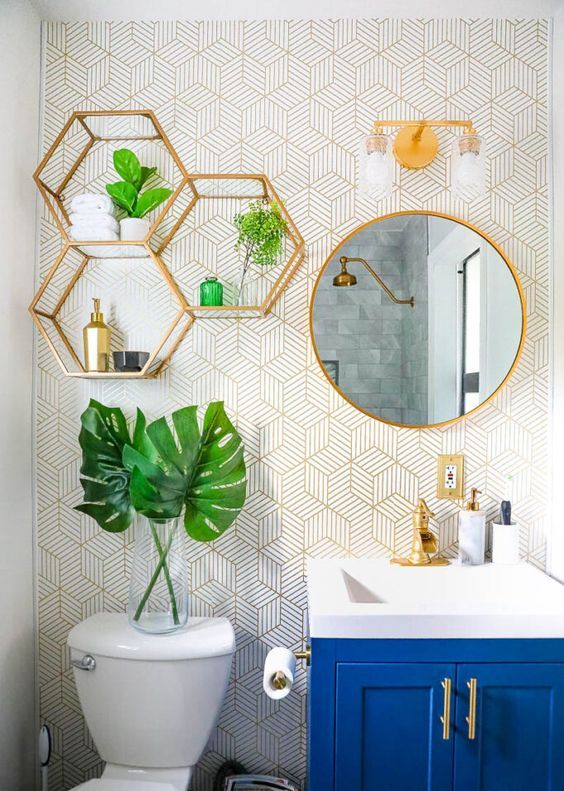 a cool bathroom with printed wallpaper, gold hexagon shelves, a round mirror in a gold frame, gold fixtures and handles is very bold